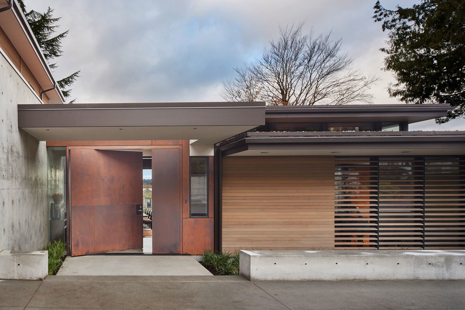 A custom Cor-Ten steel pivot door leads into the lakefront home