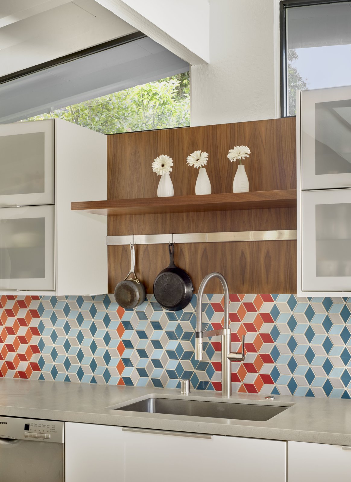 The kitchen features crisp, white cabinets, colorful mosaic tiles, and walnut accents.