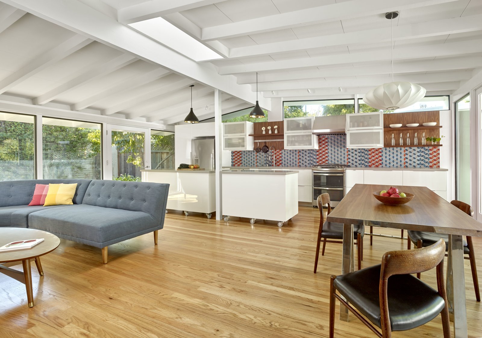 The kitchen and living area of this mid-century home features all white cabinets, light wood floors and full height windows providing plenty of natural light.