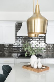 The designers refinished the existing kitchen cabinets in a crisp white and light gray accent island. They replaced the dated granite countertops with cement-colored quartz on the perimeter and marble-veined quartz as an accent on the island. These elements helped lighten up the space, as they were keeping the existing backsplash intact. The dusty blue stools and brass pendants add depth and character to the space.