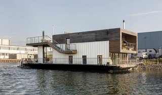 The ship-like floating home comprises a two-story cuboid sitting atop a V-shaped platform that resembles the hull of a boat. Its gangway-style external staircases add to the nautical look, as does the chimney of the wood-burning stove, which pops out of the roof terrace to recall the funnel of a ship.