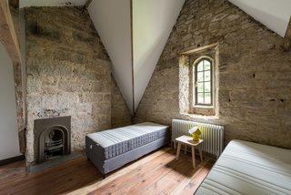 With its vaulted ceiling, tall narrow window, and exposed stone walls, this bedroom has the feeling of a convent or church building.