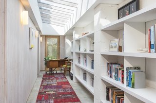 With a slanted glazed ceiling, a white fitted bookcase, and wood-clad walls, the study is a light, bright space to work in, and has views of the garden thanks to the expansive glass doors.