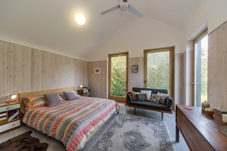 Thanks to the three glazed doors, it is now possible to see the peaceful pond and woodland from the bedroom in the master suite, which is housed in the new extension. With its simple, sloped roof, this part of the house has the form of an agricultural barn. To elongate the ceiling height, the doors finish above the blonde wood panelling.