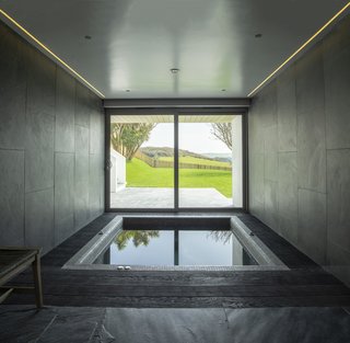 With dark gray tiles that mimic stone and atmospheric lighting, this cave-like space has a soothing feel while evoking elemental landscapes. The picture window provides scenic views of the garden, grassland, and the hills beyond while you relax in the spa bath.