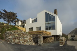 The lower-ground floor and the walls supporting the raised front garden are clad in stone, making it look like it is perched on a rock.