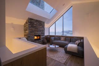 The chimney is clad in stone, with a fireplace on each floor, and can be seen through the large skylight in this living space.