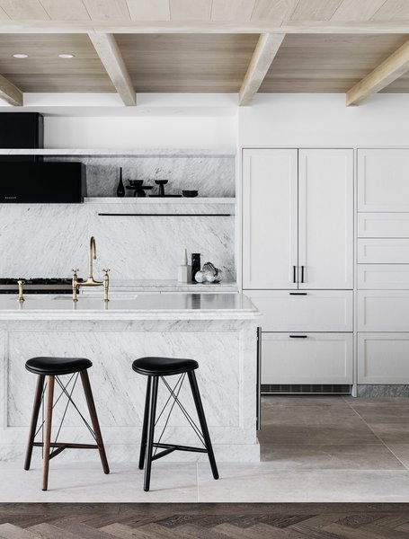 A marble island and white cabinetry define the bright, open kitchen, while matte black and bronze finishes celebrate craftsmanship.