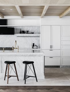 A marble island and white cabinetry define the bright, open kitchen, while matte black and bronze finishes celebrate craftsmanship. 