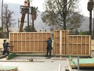 Workers unload systems-built panels and carefully assemble the shell. The crew fastens panels to the concrete slab with seismic hold downs. 