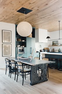 In the kitchen, statement lighting by Nuevo Living, blue-green cabinets, and an intricately carved wooden table juxtaposes modern living with rustic touches.