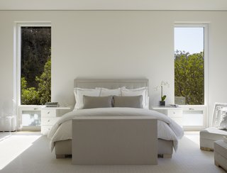 The sleek master bedroom is outfitted in fresh whites and tonal grays, giving the rustic space a modern feel.
